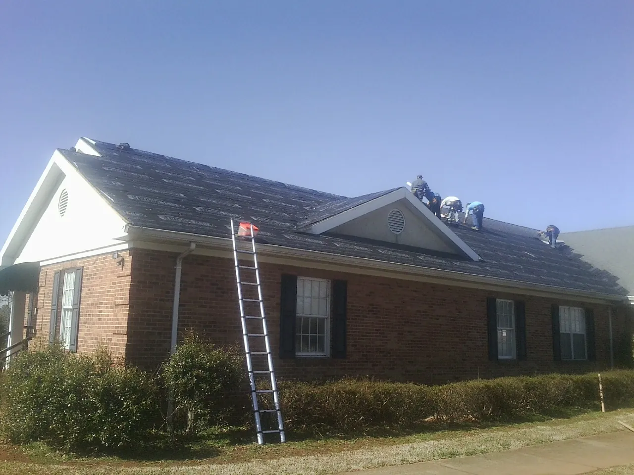 Crew tearing shingles off a brick ranch roof with a ladder set — Metal Roof Repair work by our crew in Loomis