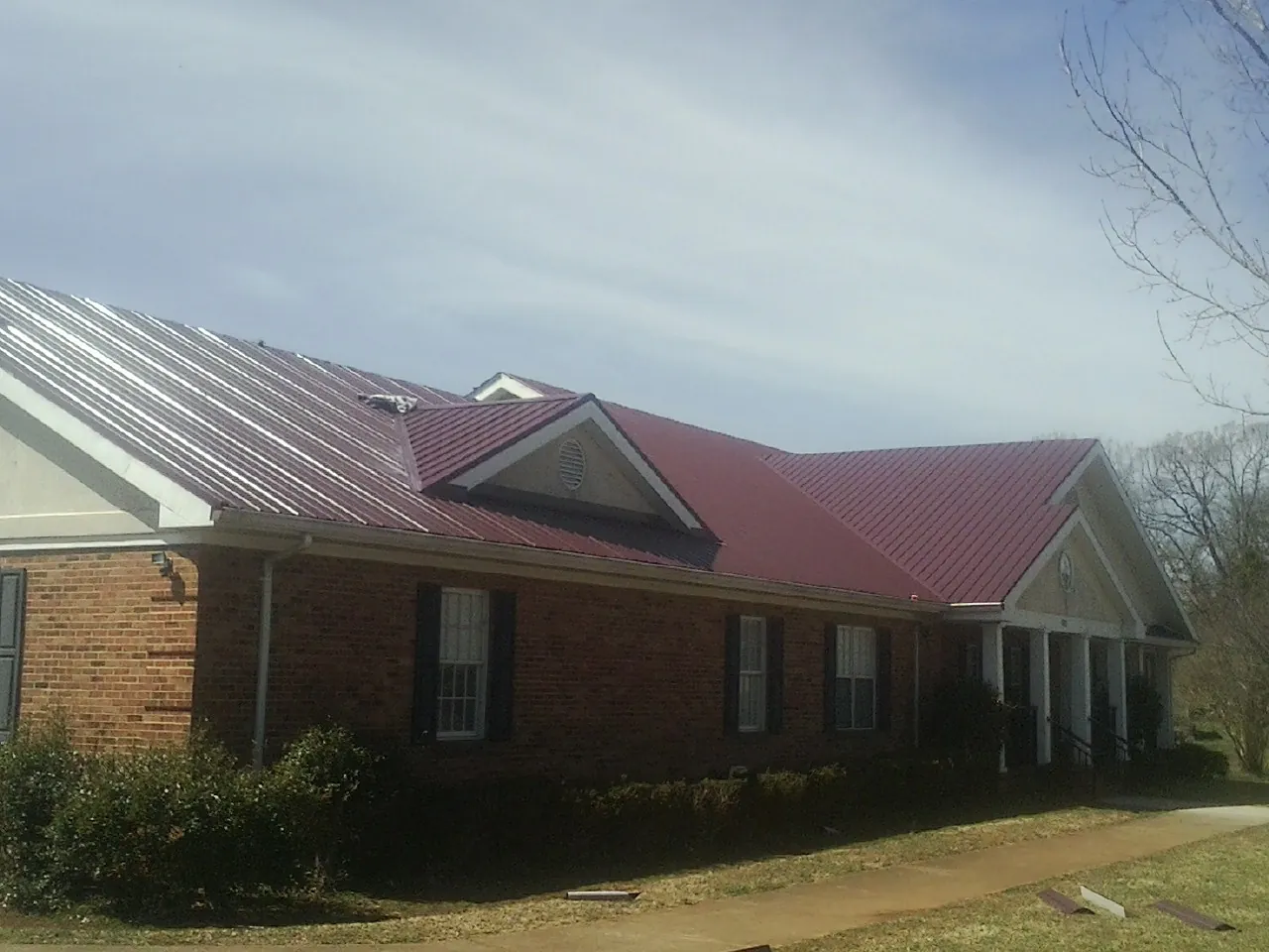 Red metal roof with gabled entries on a long brick building, from a Hail Damage Roof Repair job in Loomis