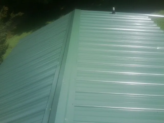 New green metal panels meeting at the ridge of a roof — Flat Roof Repair work by our crew in Loomis