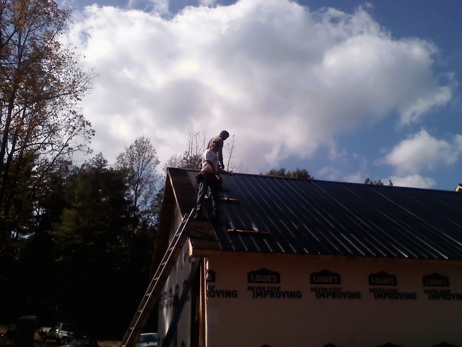 Roofer fastening dark metal panels high against a cloudy sky, from a Roof Inspection job in Loomis